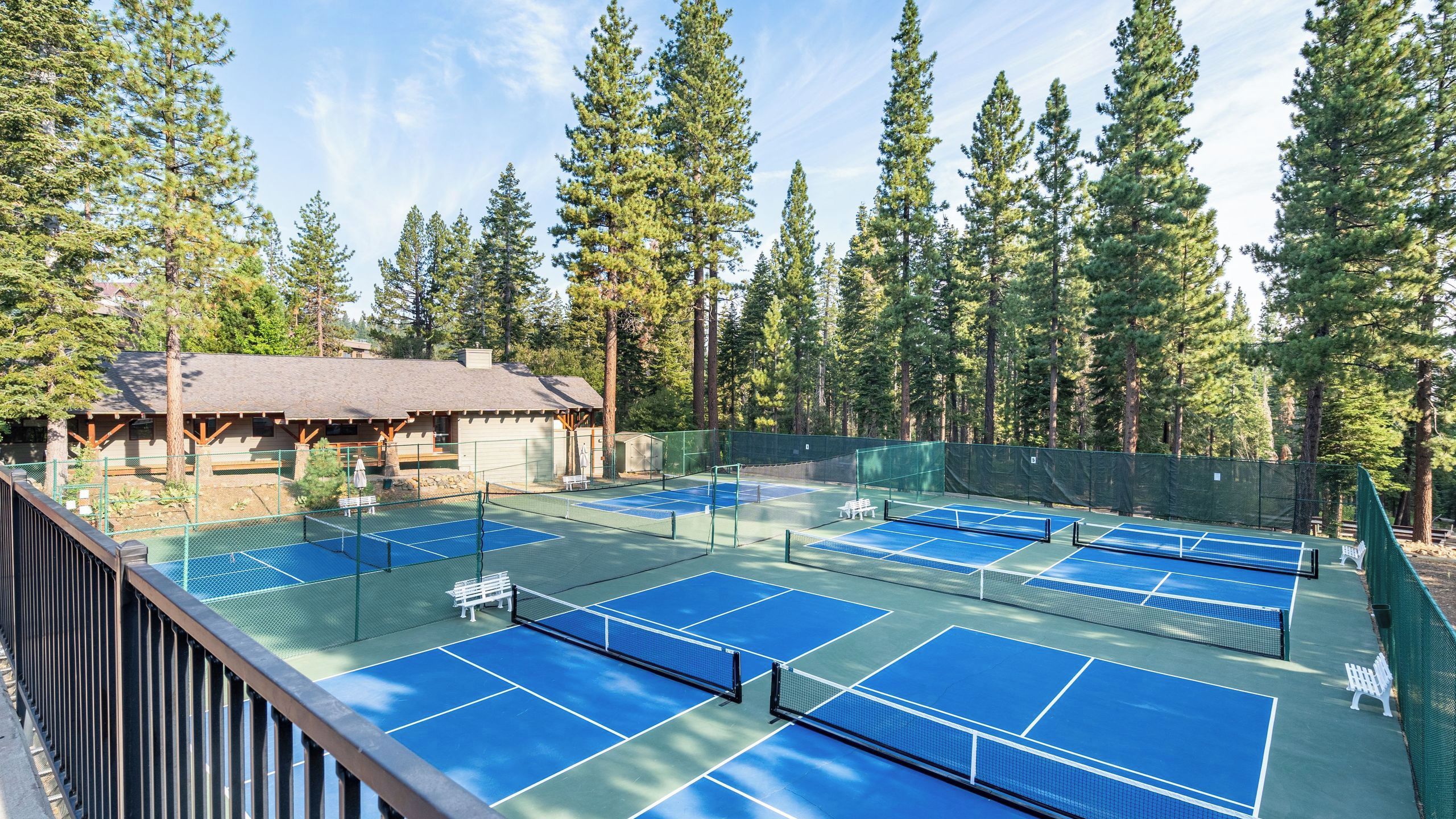 Un campo da tennis con più campi, circondato da alberi alti e un padiglione con tetto di paglia.