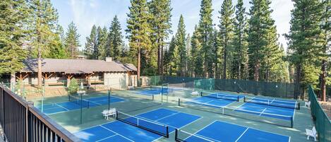 Canchas de tenis múltiples, rodeadas por altos árboles y una cabaña con techo de paja.