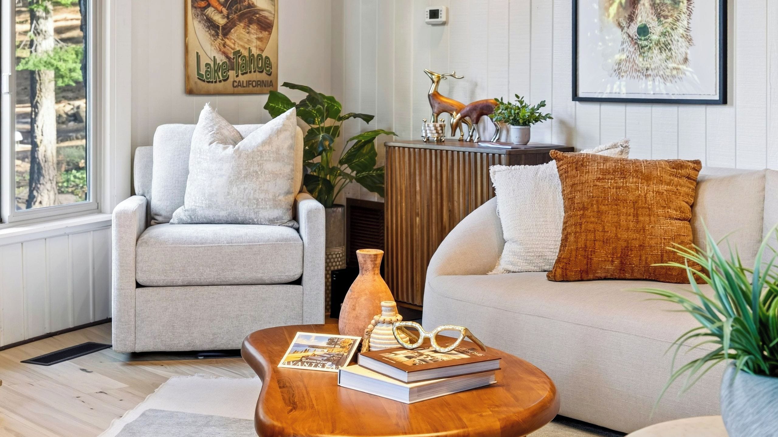 A living room with a grey armchair, a beige sofa, and a wooden coffee table with books and glasses.