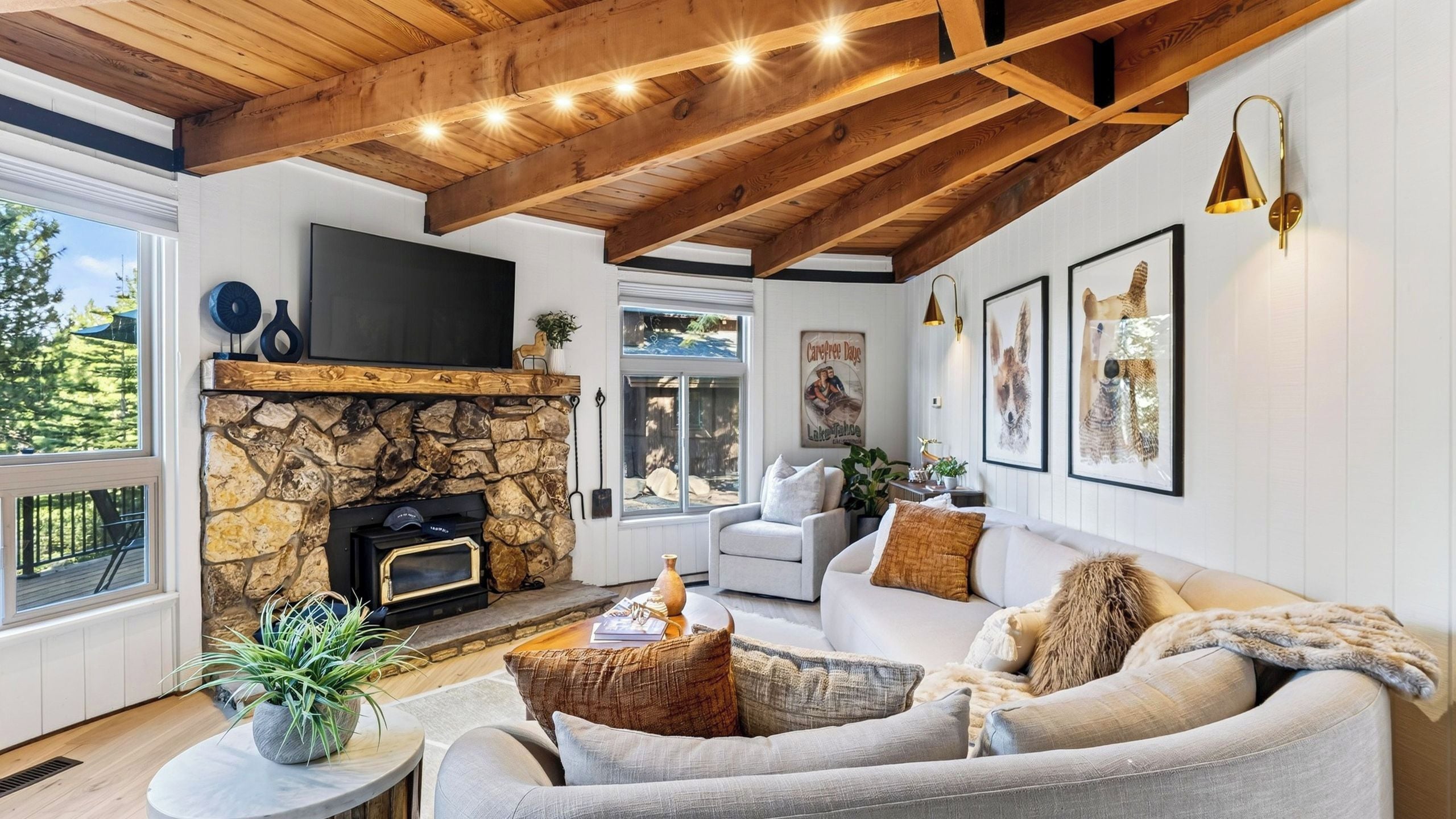 A living room with a stone fireplace, a flat-screen TV, a sofa set, and artwork on the walls.