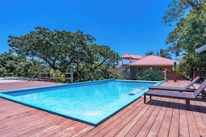 A rectangular swimming pool with a wooden deck, surrounded by trees and a building with a red roof. - Your Own Private Resort in Roatán! (José Santos Guardiola)