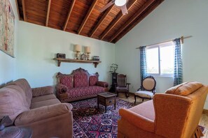 A room with a high wooden ceiling, a patterned rug, a sofa, a chair, and a window with curtains. - Your Own Private Resort in Roatán! (José Santos Guardiola)