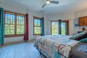 A bedroom with a bed, two windows with curtains, a ceiling fan, and a view of trees. - Your Own Private Resort in Roatán! (José Santos Guardiola)