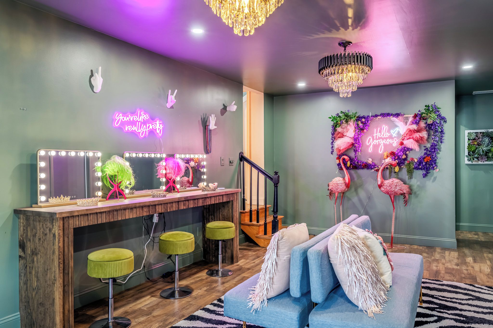 A room with a vanity area, a staircase, and a seating area with a decorative wall.