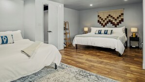 Quarto com duas camas, piso de madeira, tapeçaria na parede e uma escada encostada à parede.