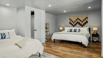 A bedroom with two beds, a wooden floor, a wall-mounted tapestry, and a ladder leaning against the wall.