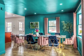 A dining area with a teal-colored wall, a wooden floor, and a table set for four with pink and blue chairs. - Neon & Pop Retro Cabin w/ Sauna and Hot Tub
Neon & Pop (East Stroudsburg)