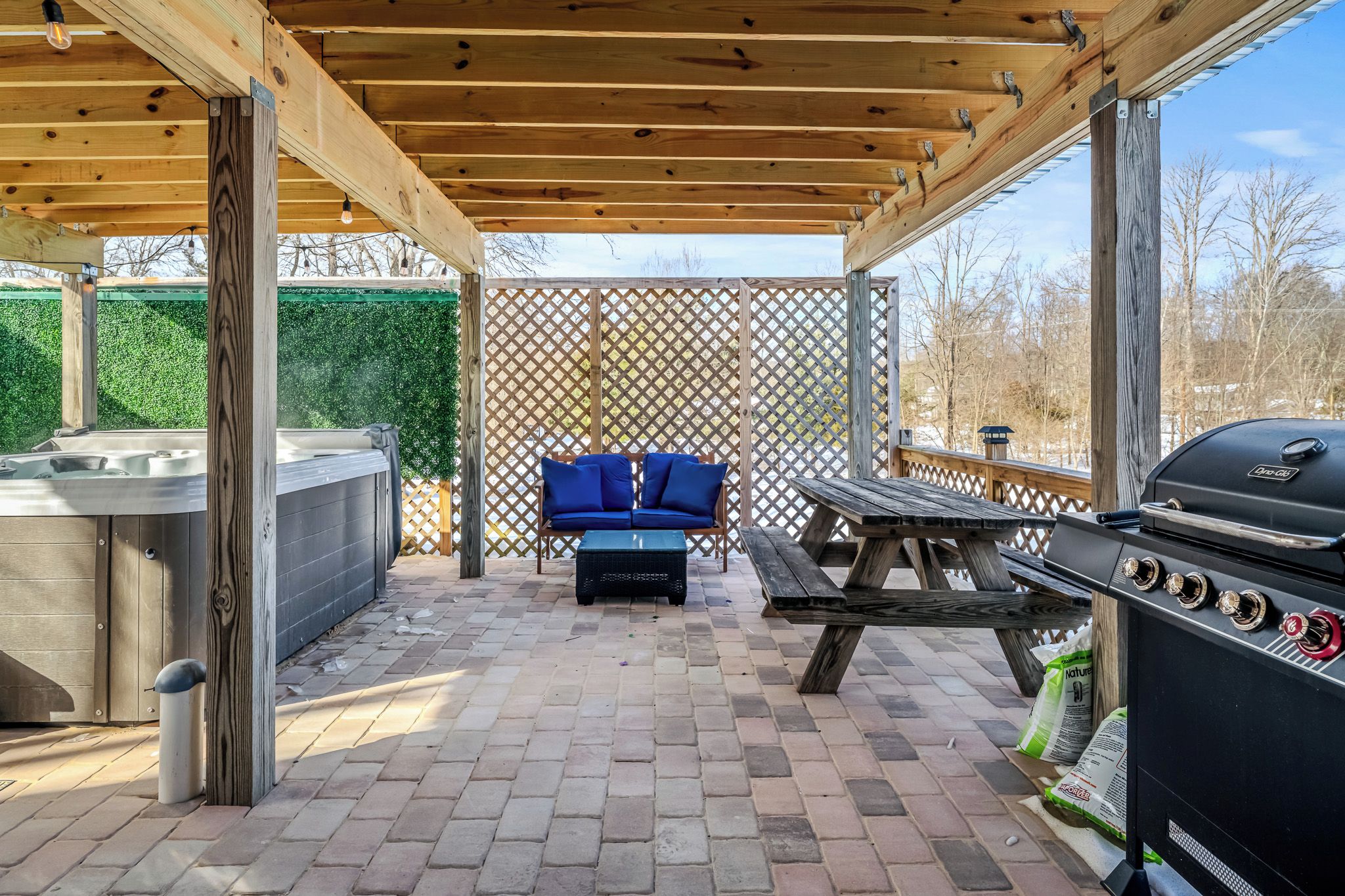 An outdoor patio with a hot tub, a barbecue grill, and a seating area with blue cushions.