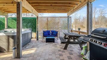 An outdoor patio with a hot tub, a barbecue grill, and a seating area with blue cushions.