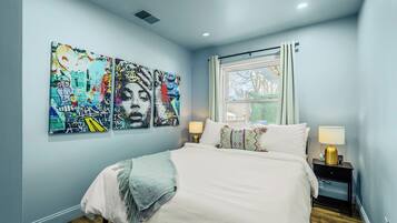 A bedroom with a bed, two bedside tables, a window, and three wall-mounted artworks.