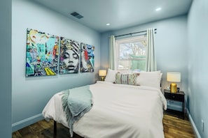 A bedroom with a bed, two bedside tables, a window, and three wall-mounted artworks.