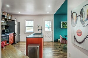 A modern kitchen with a central island, a dining area with a teal accent wall, and a large window providing natural light.