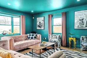 A teal-colored room with a pink sofa, a coffee table, and a patterned armchair. There are two windows with curtains, a framed newspaper on the wall, and a small table with a vase. - Neon & Pop Retro Cabin w/ Sauna and Hot Tub 






Neon & Pop (East Stroudsburg)