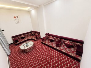A room with a patterned red carpet, two patterned sofas, a small white table, and a wall-mounted artwork. - Pissonia Furnished Apartments (Addis Ababa)