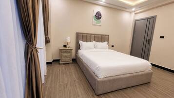 A bedroom with a bed, nightstand, curtains, and a wall-mounted artwork.