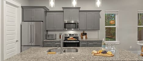 A modern kitchen with granite countertops, stainless steel appliances, and pendant lighting.