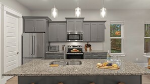 A modern kitchen with granite countertops, stainless steel appliances, and pendant lighting. - Maré 33 by Avantstay 6-seat Golf Cart + Arcade + Bunk Room Beach Walk + Pool (Miramar Beach)