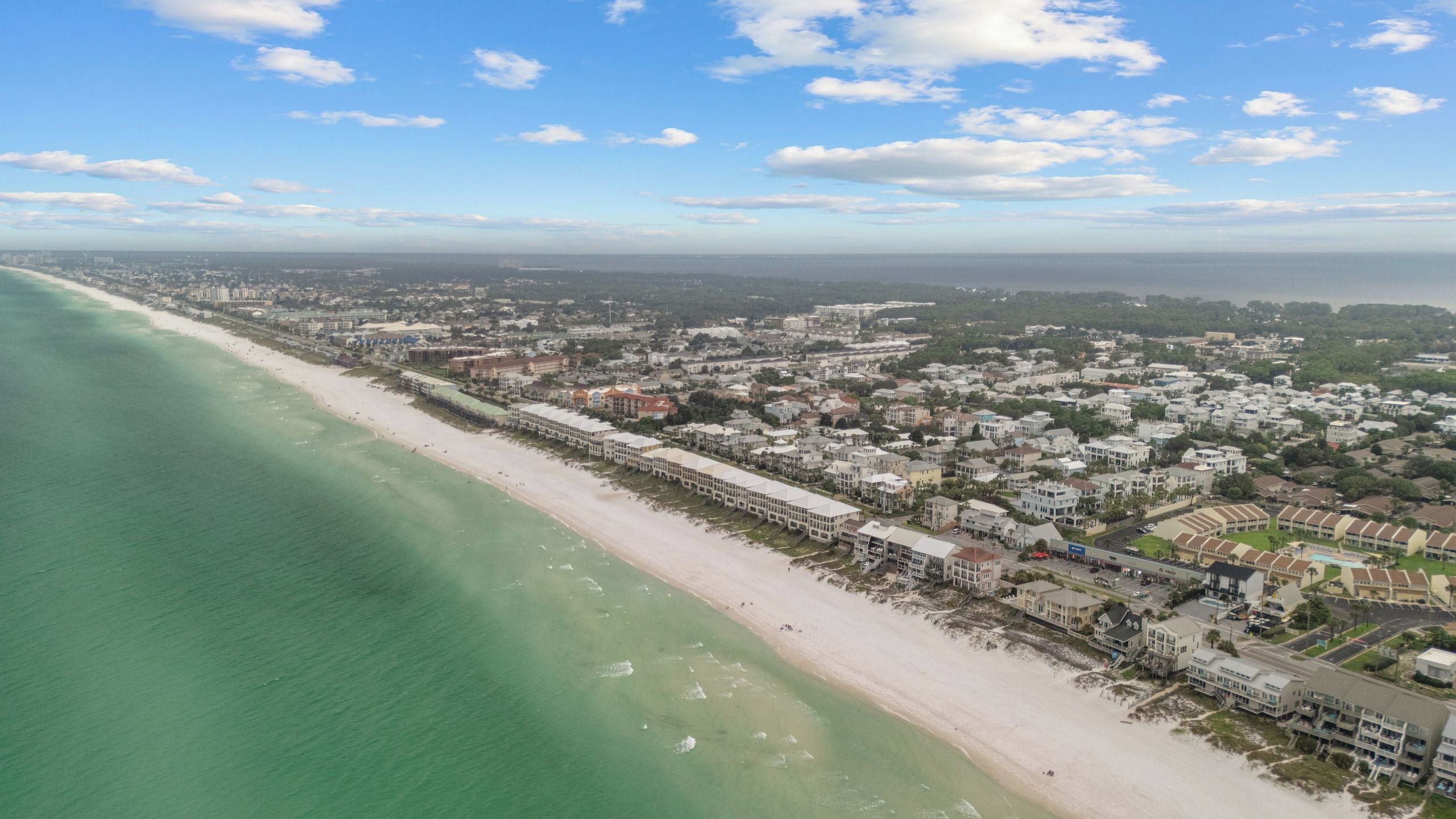 An aerial view of a coastal town with a beach, buildings, and a clear sky.