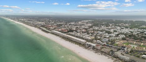 An aerial view of a coastal town with a beach, buildings, and a clear sky.