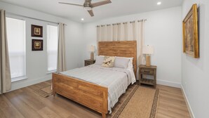 Une chambre à coucher avec un lit en bois, deux tables de chevet avec des lampes, un ventilateur de plafond et une fenêtre avec des rideaux.