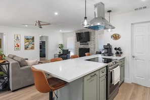 Una cocina moderna con una isla central, un área de comedor con un sofá y un televisor montado en una pared de ladrillo.