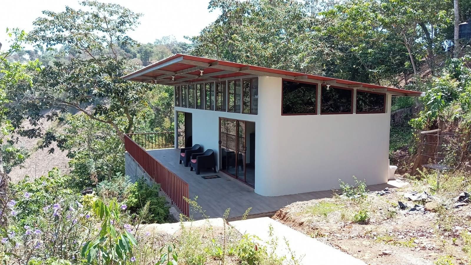 Un bâtiment moderne, de plain-pied, doté d’un toit plat et de grandes fenêtres, entouré d’une végétation naturelle.