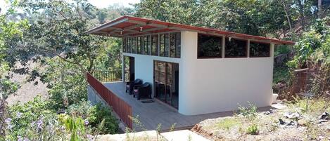 Un edificio moderno de un piso con techo plano y amplios ventanales, rodeado de vegetación natural.