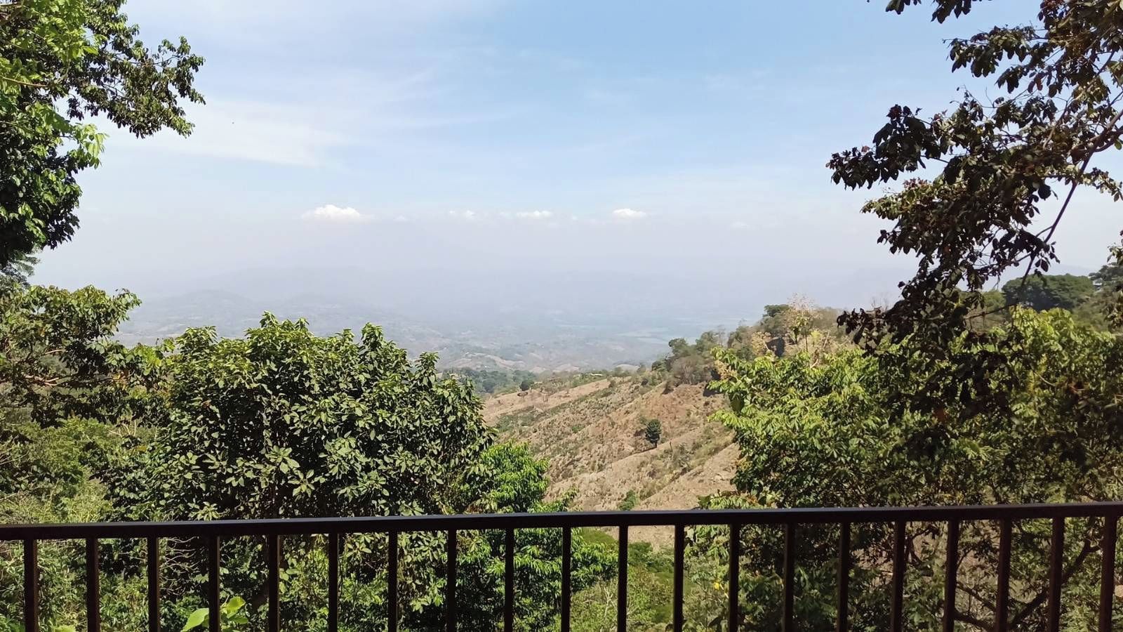 Vista desde un balcón con barandilla, sobre un paisaje montañoso de vegetación densa y cielo despejado.