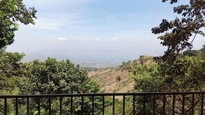 Vista desde un balcón con barandilla, sobre un paisaje montañoso de vegetación densa y cielo despejado.