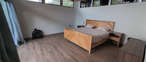 A bedroom with a wooden bed, a nightstand, a wooden wardrobe, and a window with a view of trees.
