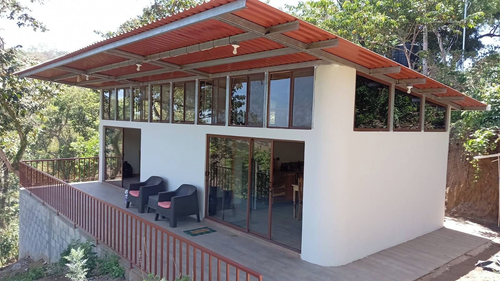 Un edificio moderno de dos pisos con un balcón, ventanas grandes y techo rojo.