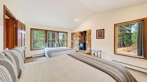Quarto com cama grande, lareira de pedra e vista para árvores pelas janelas.