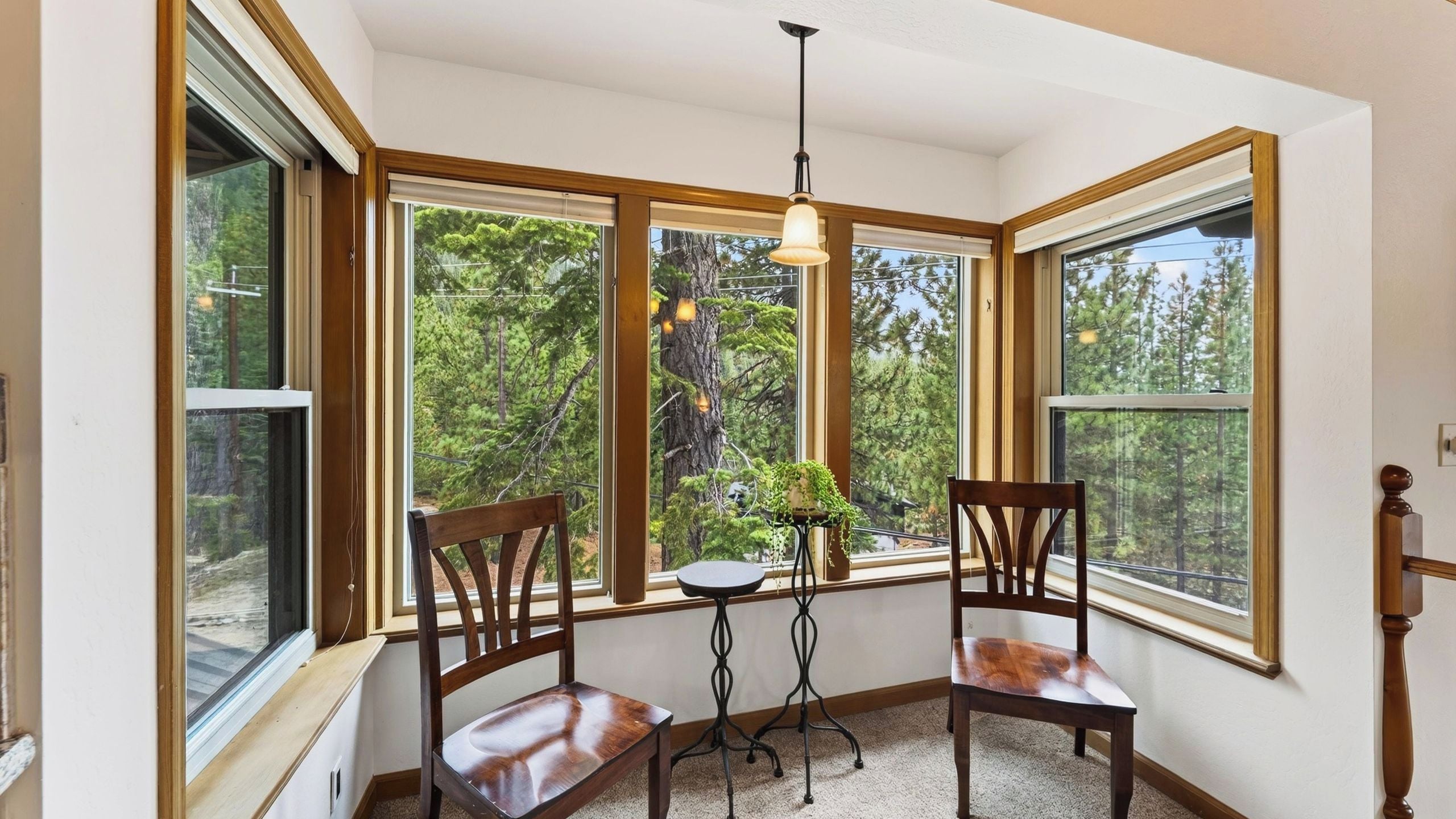 A room with large windows, two wooden chairs, a small table, and a hanging light fixture.