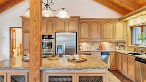 A kitchen with wooden cabinets, granite countertops, stainless steel appliances, and a hanging light fixture.