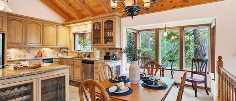 A kitchen with wooden cabinets, a dining area with a table set for four, and large windows offering a view of trees.