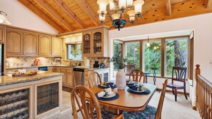 A kitchen with wooden cabinets, a dining area with a table set for four, and large windows offering a view of trees.
