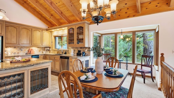 A kitchen with wooden cabinets, a dining area with a table set for four, and large windows offering a view of trees.