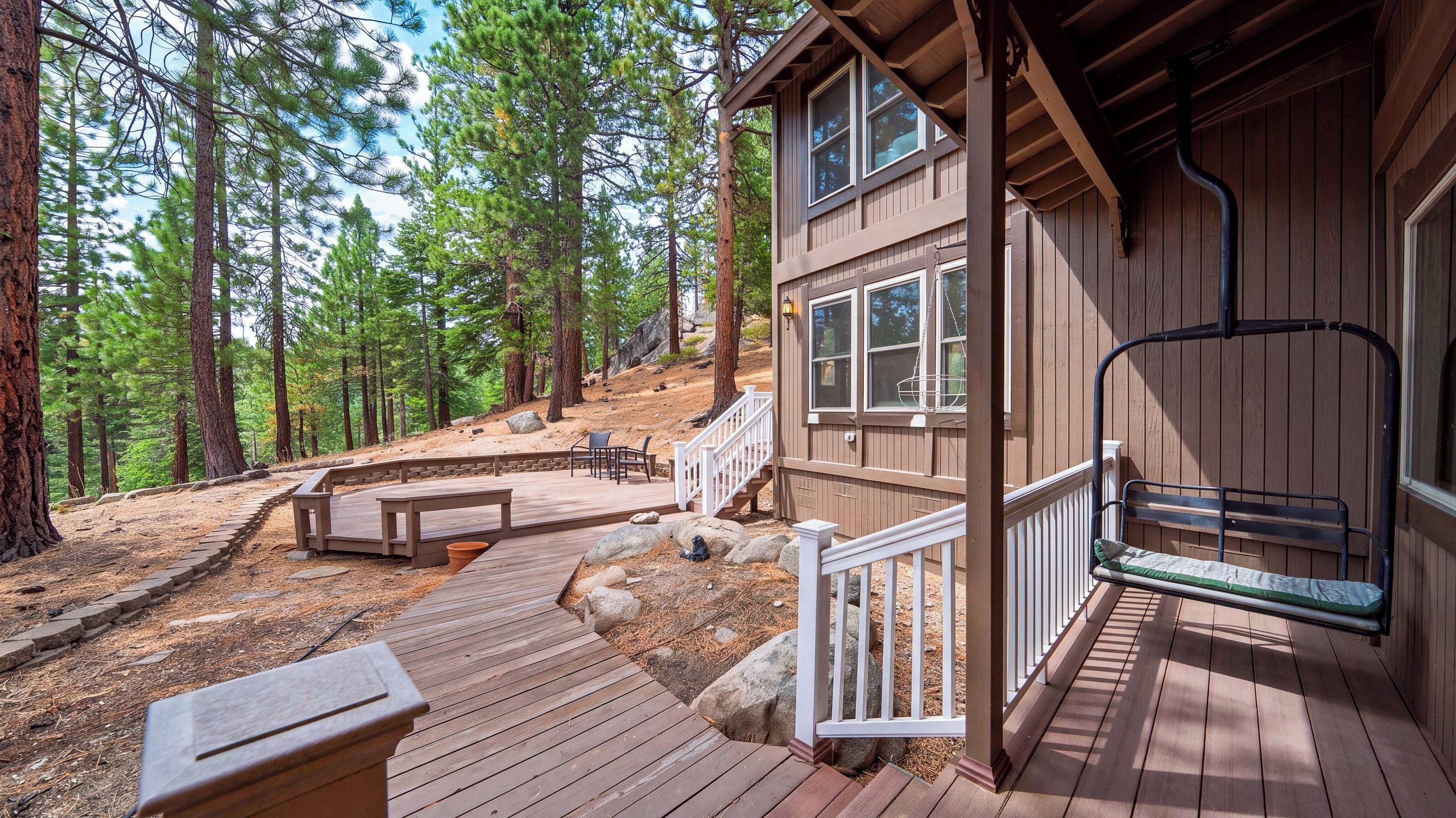 A wooden cabin with a deck, outdoor seating, and a staircase leading to a porch.