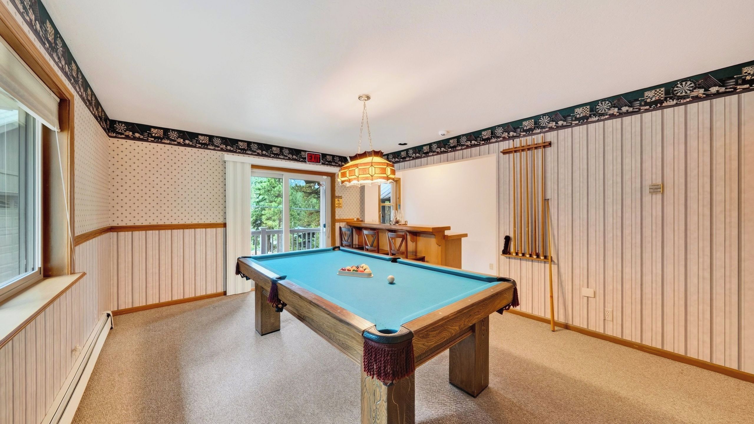 A pool table in a room with wooden paneling, a hanging light fixture, and a door with vertical stripes.