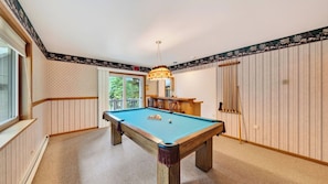 A pool table in a room with wooden paneling, a hanging light fixture, and a door with vertical stripes.