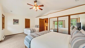 Quarto com uma cama grande, uma cama menor, ventilador de teto, um quadro e vista para o exterior pela janela.