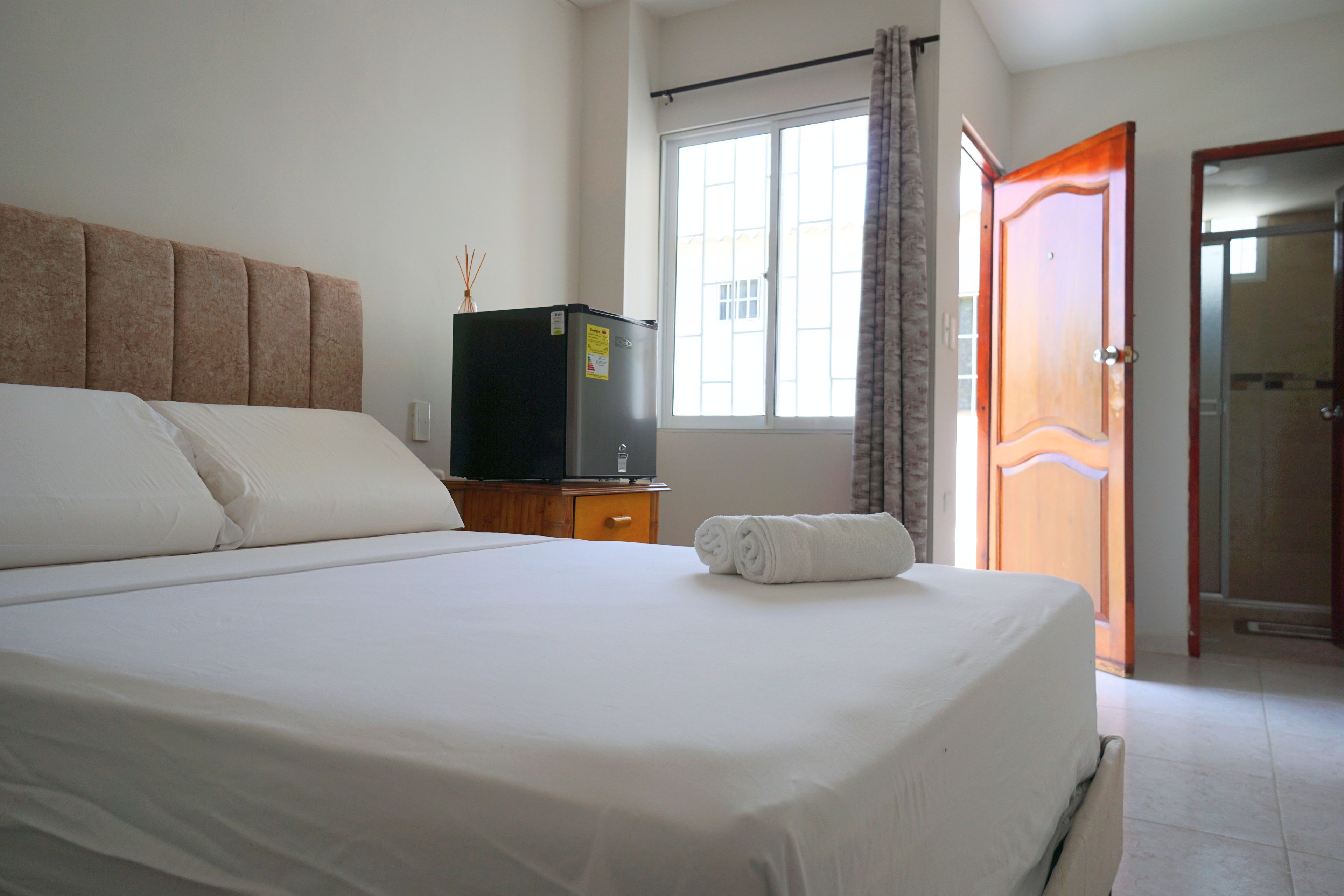 A hotel room with a bed, a television on a wooden cabinet, a window with curtains, and a door.