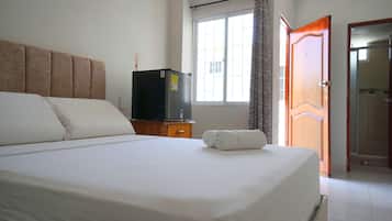 Una habitación de hotel con una cama, un televisor sobre un mueble de madera, una ventana con cortinas y una puerta.
