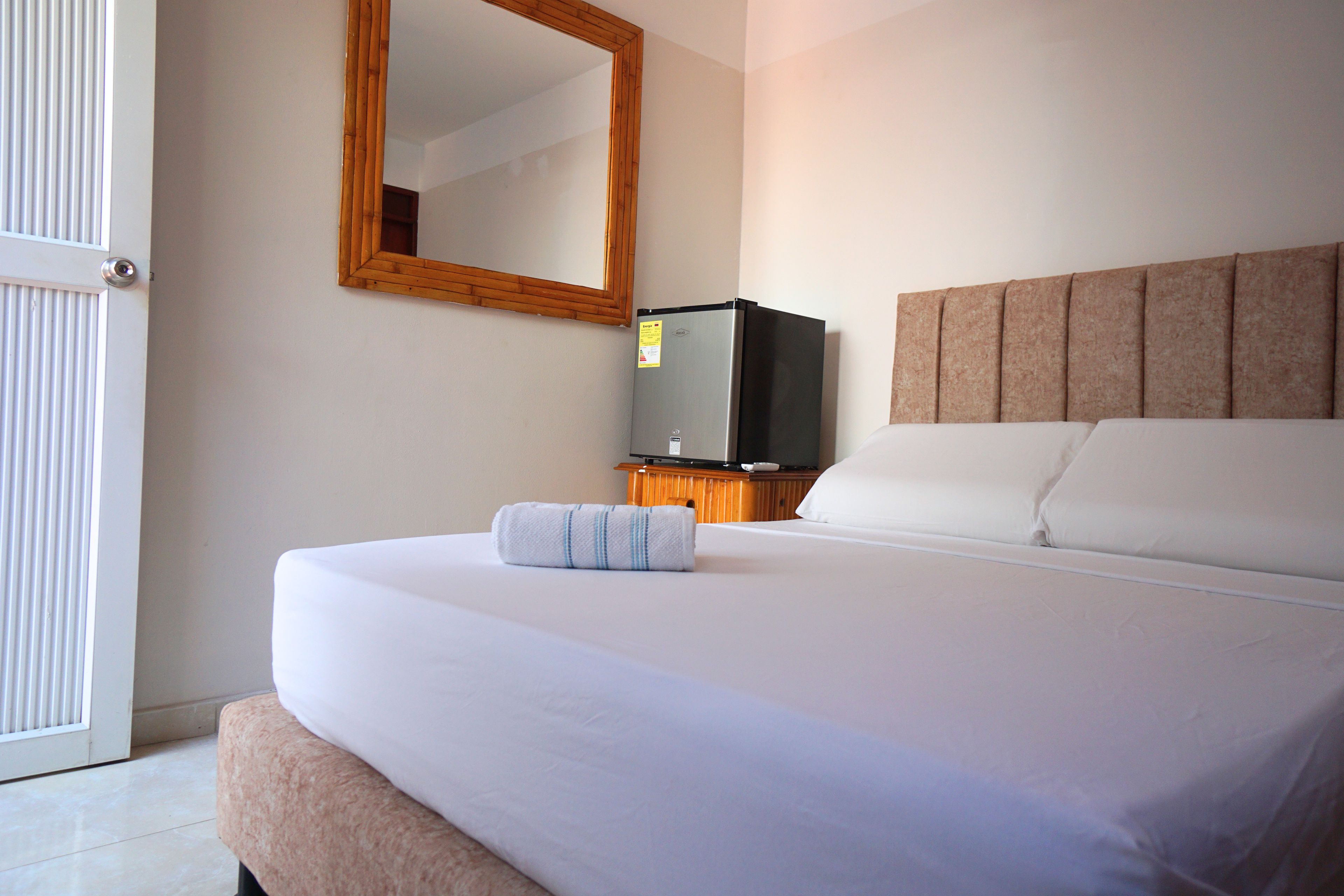 A hotel room with a bed, a television on a wooden stand, a mirror on the wall, and a door.