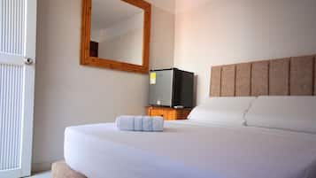 Una habitación de hotel con una cama, un televisor sobre un soporte de madera, un espejo en la pared y una puerta.