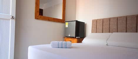 Una habitación de hotel con una cama, un televisor sobre un soporte de madera, un espejo en la pared y una puerta.