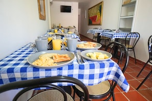 Una zona de menjador amb taules de taula escacarrada, plats de menjar i un televisor fixat a la paret.