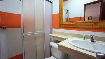 A bathroom with a shower, toilet, sink, and a mirror with a wooden frame.