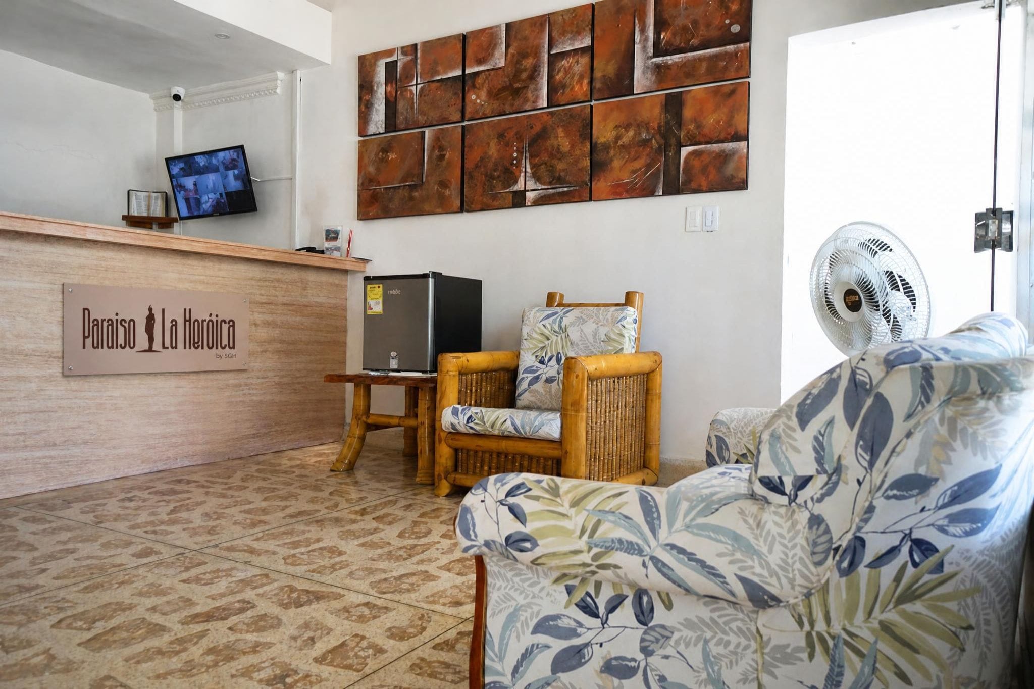 A reception area with a wooden desk, a television, a wall-mounted artwork, and a fan.