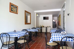 Un comedor con mesas cubiertas por manteles a cuadros azules y blancos, sillas negras y piso de baldosas.